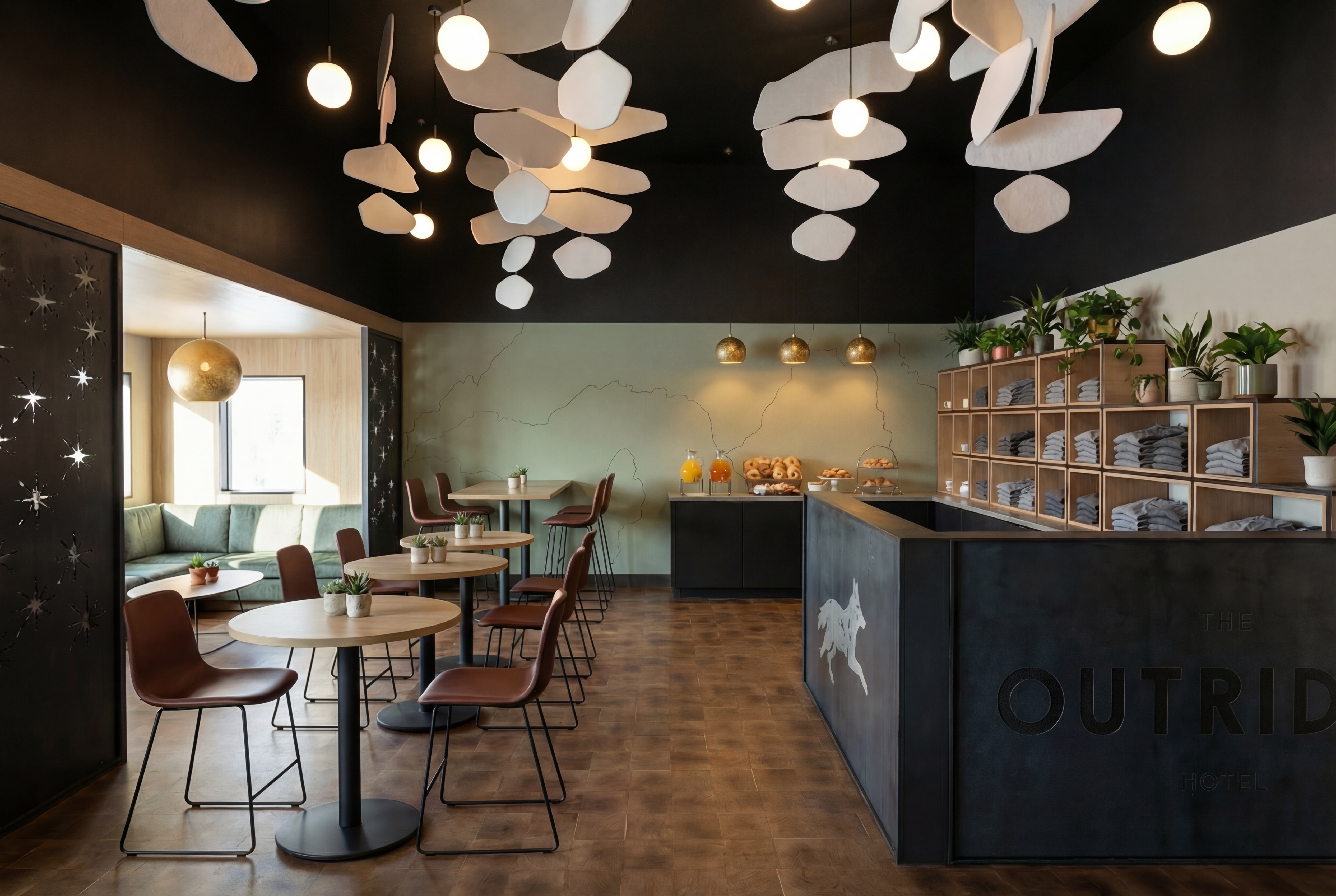 The Outrider Hotel lobby wide view with sculptural ceiling art, seating area, and continental breakfast spread